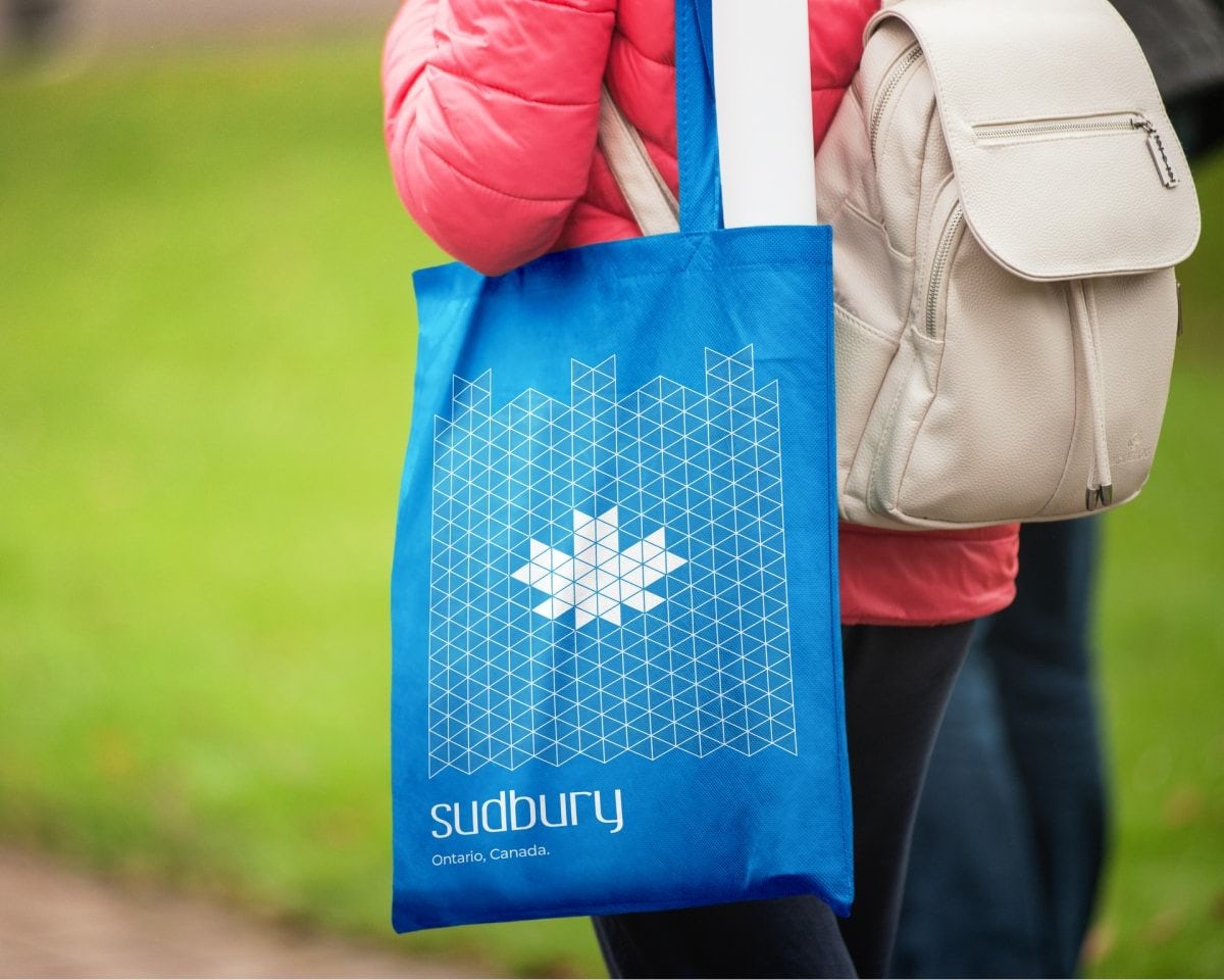 Woman holding a blue Sudbury, Ontario tote bag with Greater Sudbury Economic Development branding