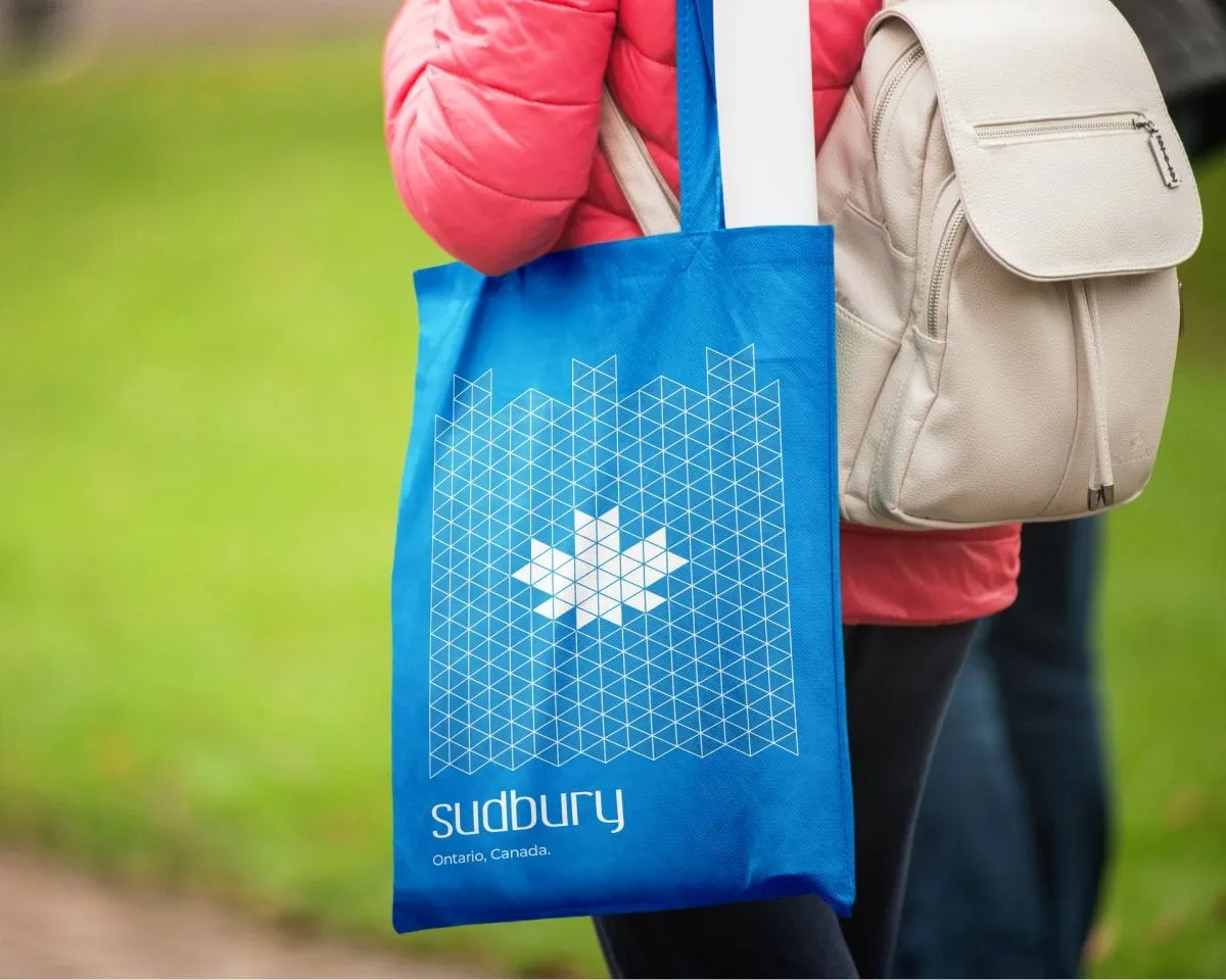 Woman holding a blue Sudbury, Ontario tote bag with Greater Sudbury Economic Development branding