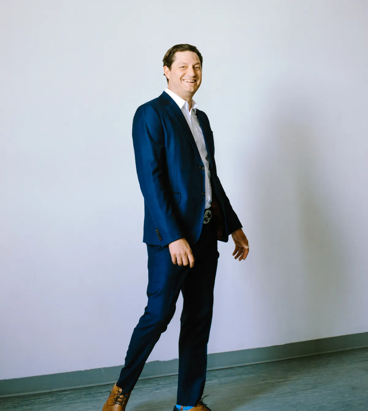 A man in a suit and tie, Ellis Boucher, stands confidently in an empty room, showcasing professionalism and readiness.