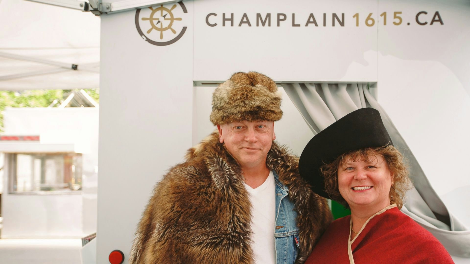 Man and women in historic costume standing in front of the Champlain1615 interactive booth