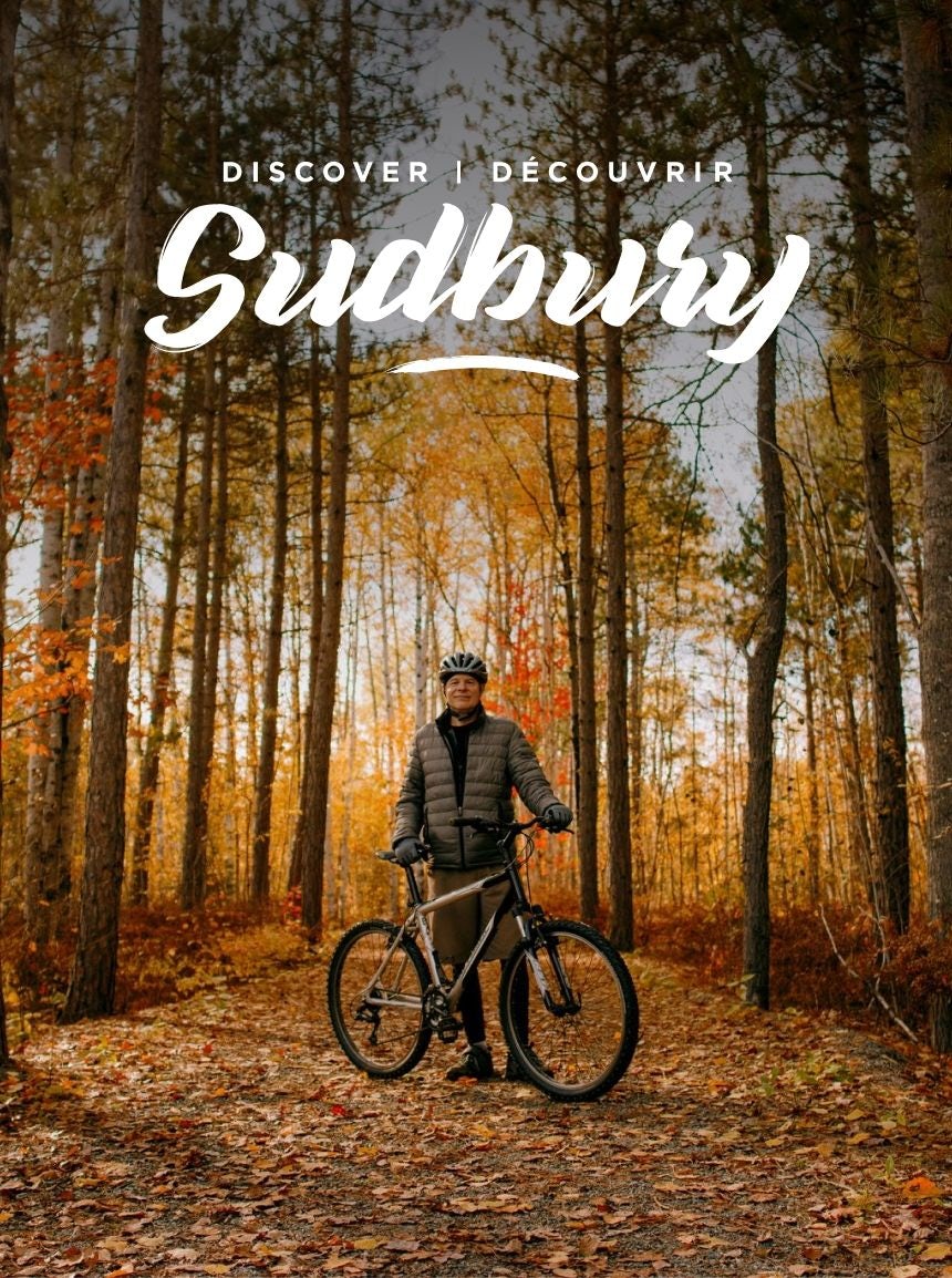Fall scene of a man standing in the forest with his mountain bike below the Explore Sudbury masthead
