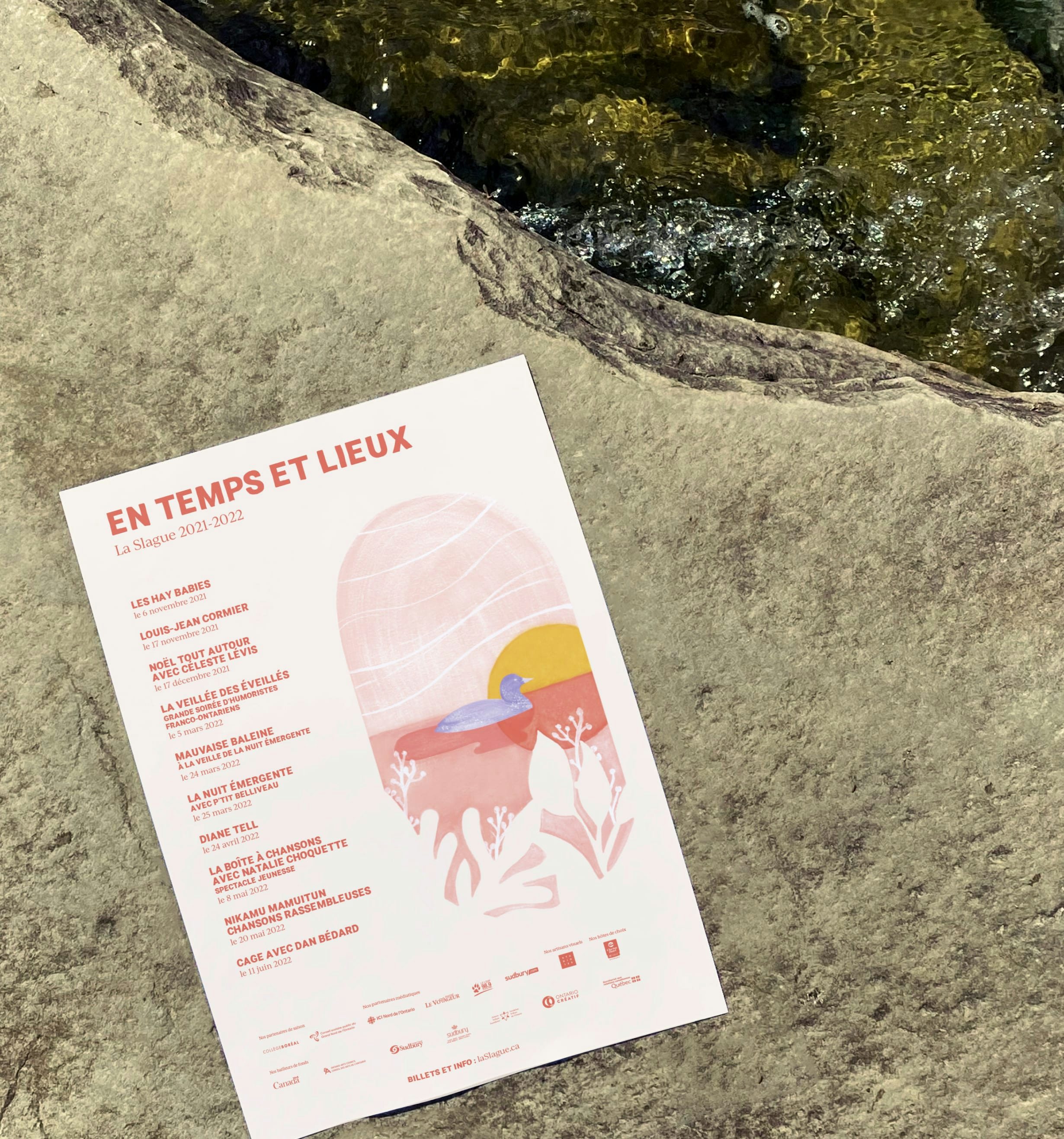 Branded poster for La Slague's 2021-2022 season placed on a rock