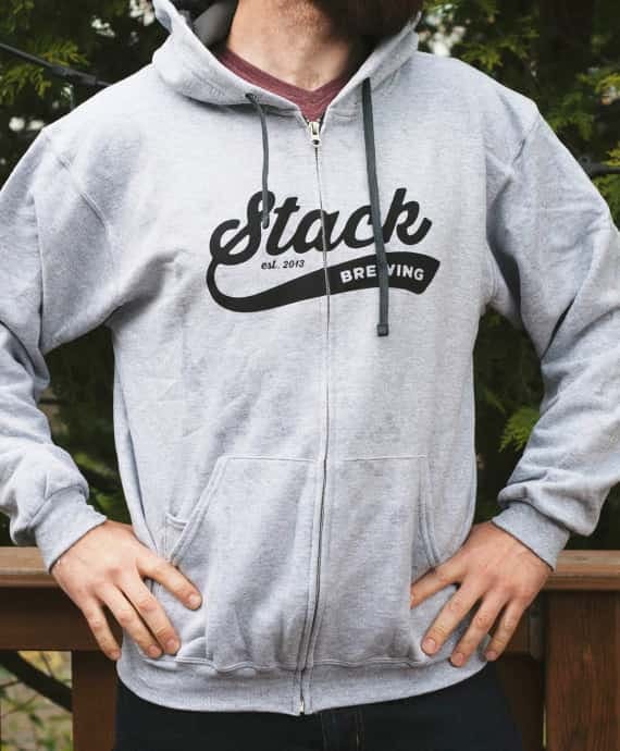 Man wearing grey Stack Brewing zip-up hoodie with scripted font on front