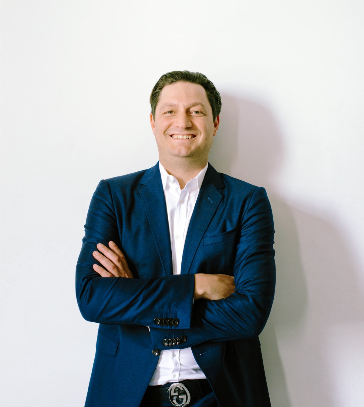 A man in a blue suit and white shirt, Ellis Boucher, owner of Ellis Realtor, stands confidently for a professional portrait.