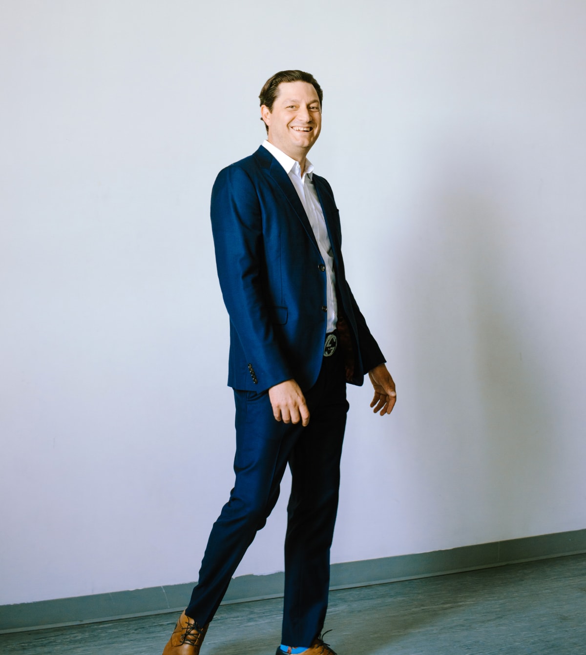A man in a suit and tie, Ellis Boucher, stands confidently in an empty room, showcasing professionalism and readiness.