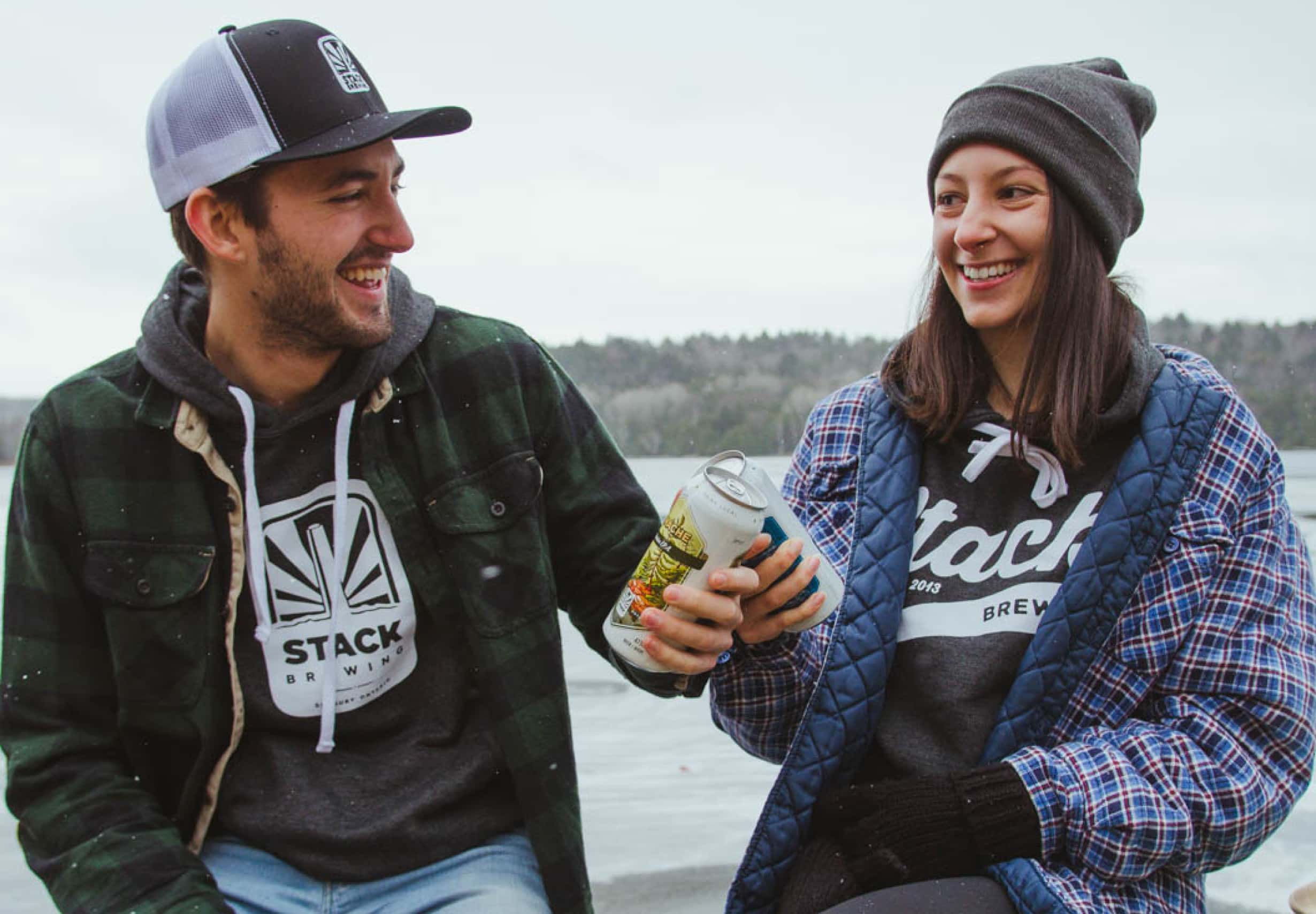 Young adults cheers two Stack beers while wearing branded hoodies in the outdoors