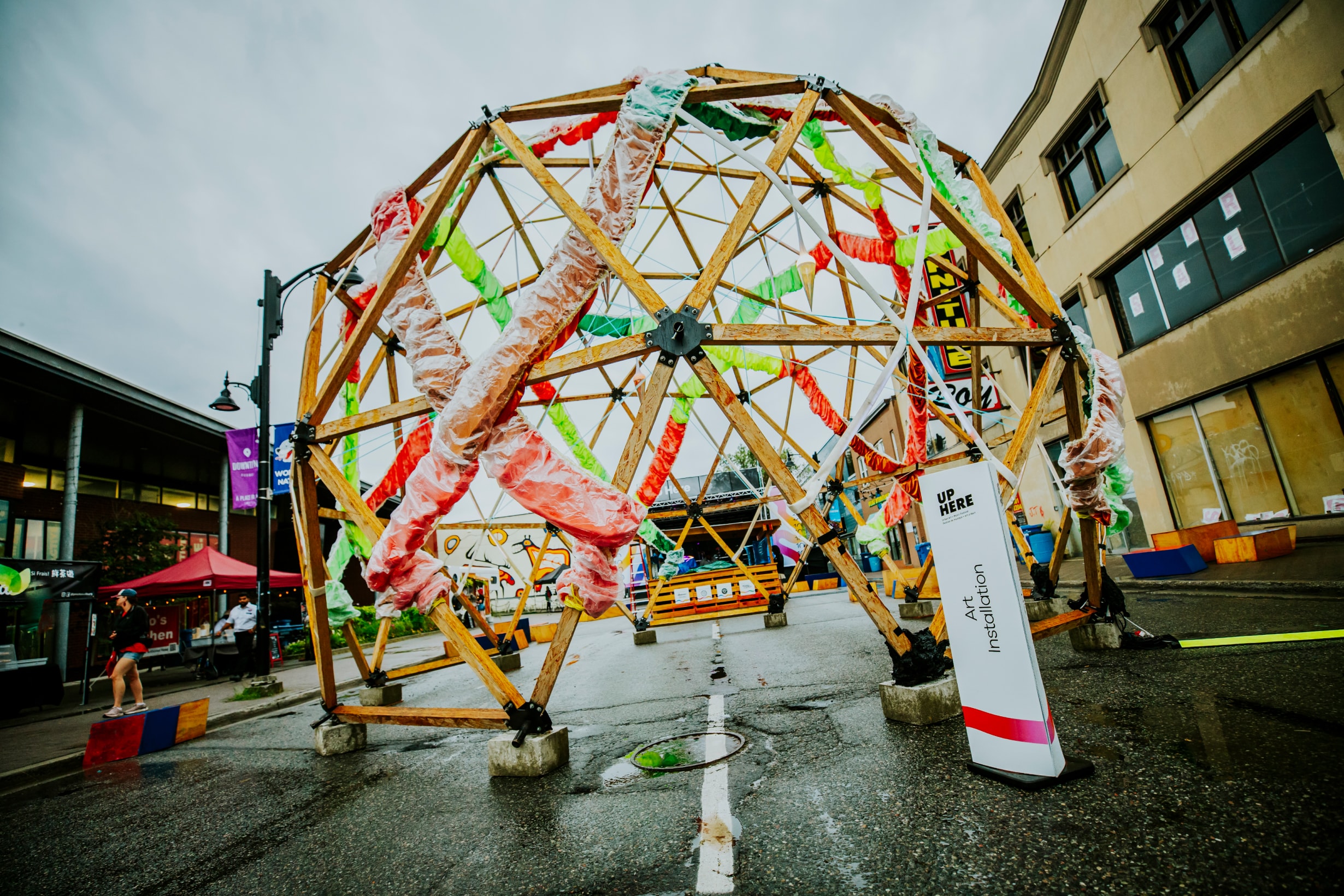 Geodesic dome wrapped in colourful fabric in middle of city street.